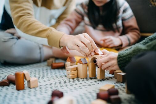Nahaufnahme von Eltern, die im Wohnzimmer auf dem Boden sitzen und zusammen mit ihrer Tochter mit Holzbausteinen spielen